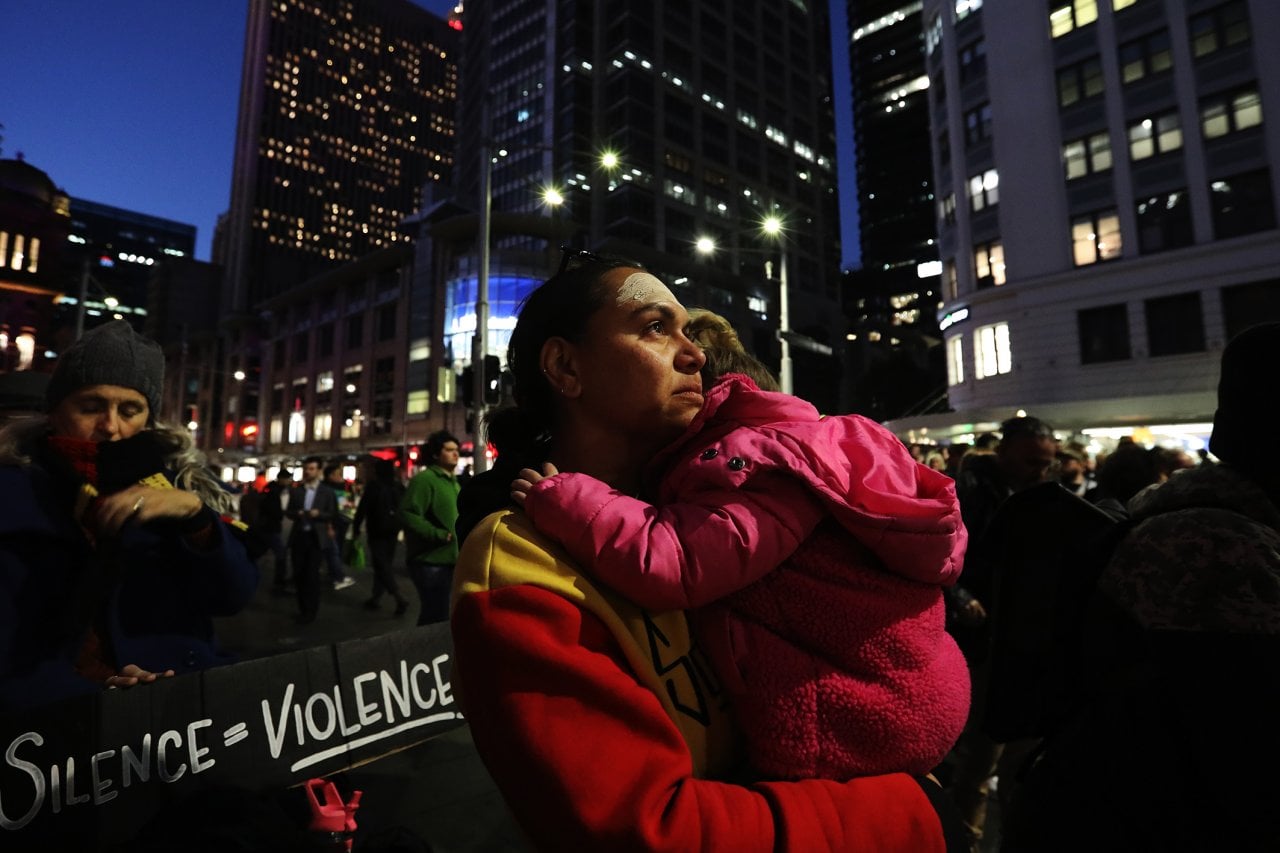 A woman holds a small child amid a street protest.