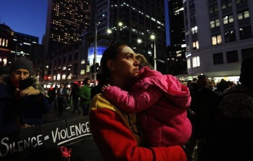 A woman holds a small child amid a street protest.