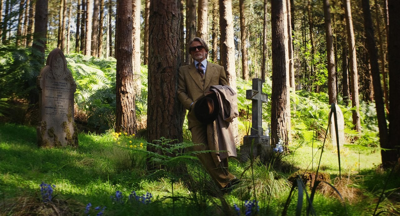 Daniel Craig as detective Benoit Blanc, standing in a green cemetery.