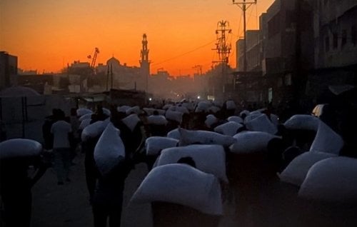 Men carry sacks of flour taken from a raided aid truck in Khan Younis, southern Gaza.
